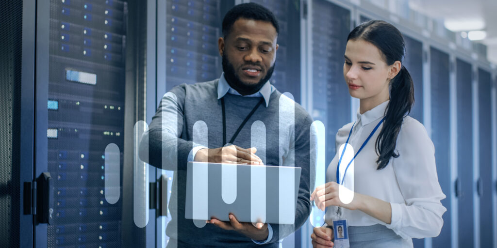 Young black man and young white woman look at a laptop while standing in a server room with wireless icon screened over top.