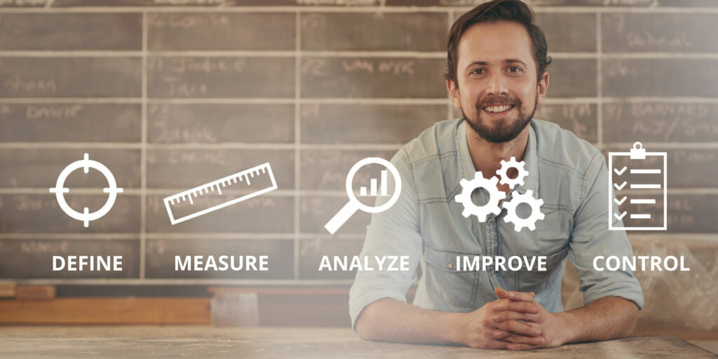 White man in a gray casual business shirt leaning on a table with a blackboard behind him with a grid. Overlaying the image are the terms define, measure, analyze, improve, and control.