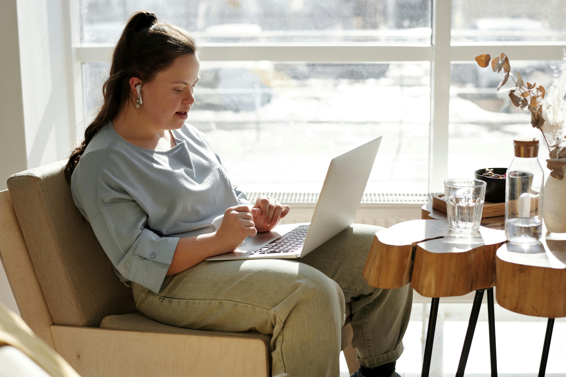 Young woman with Down's sitting in a cafe with a laptop on her lap.