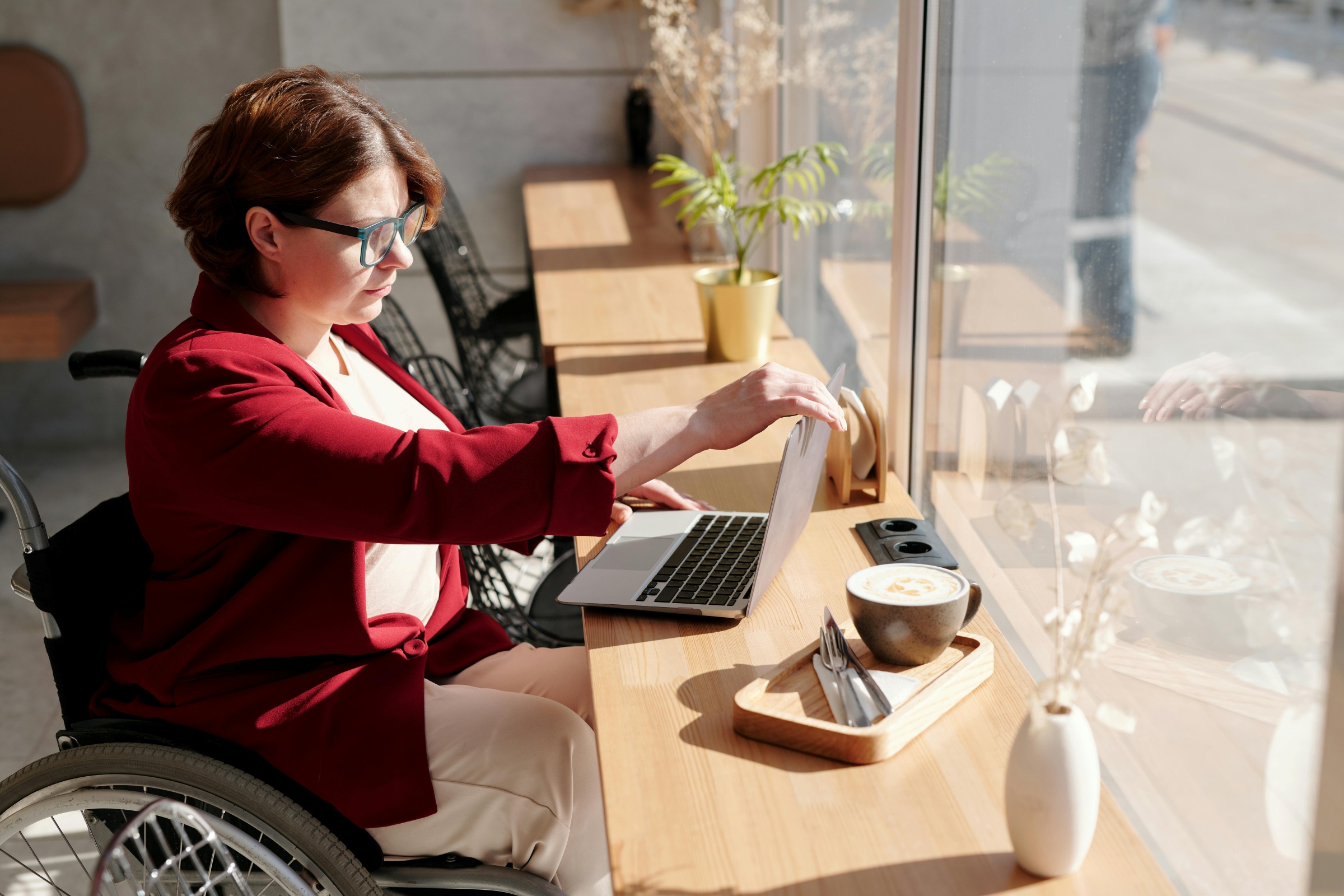 middle aged white woman in a wheelchair opening a laptop in a cafe window