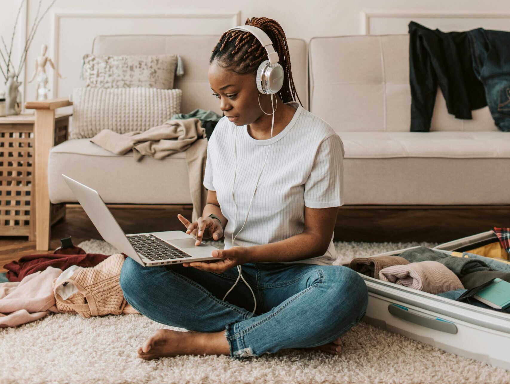Young black woman in casual clothes sitting on the floor wearing headphones and looking at a laptop.