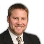 headshot of a white man with brown hair and short beard wearing a suit and tie