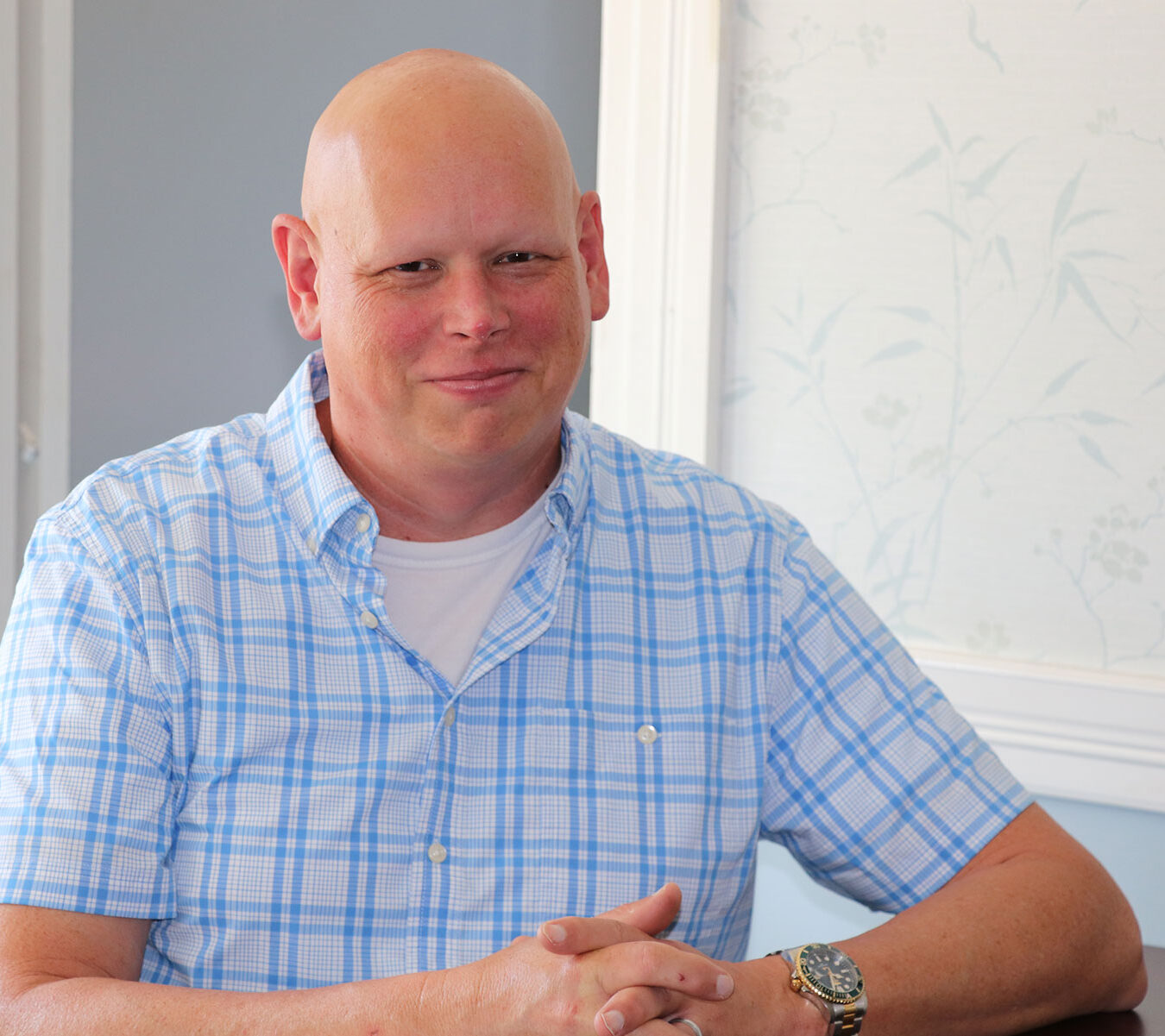 White bald man in a short sleeved blue and white checked shirt.