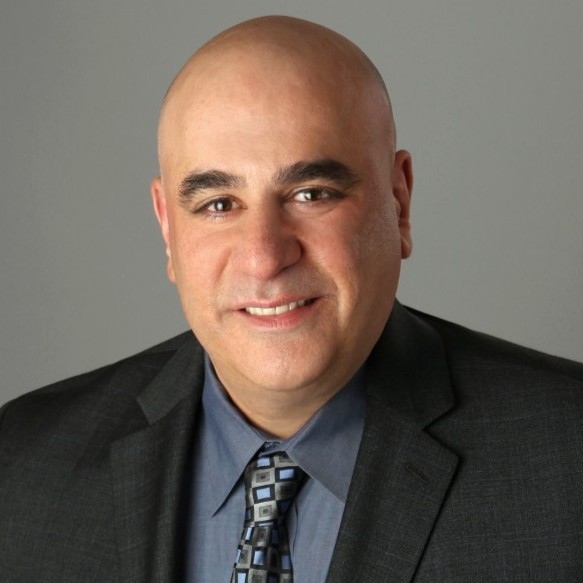 A smiling bald white man wearing a dark suit, gray shirt and tie