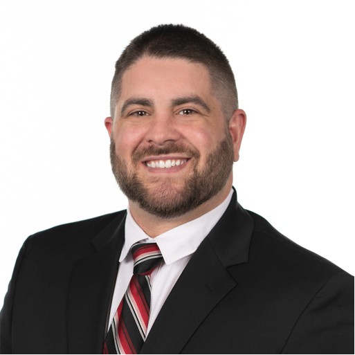 white adult male with short dark hair and close beard wearing a suite and tie